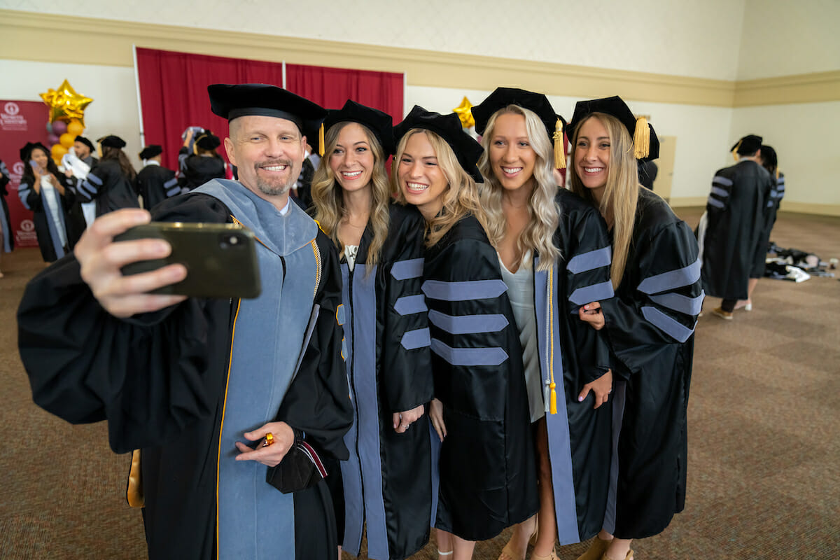 The 4th year director posing for a selfie with four Veterinary Medicine Graduates. All are wearing academic regalia with grey velvet to symbolize veterinary medicine. The 4th year director posing for a selfie with four Veterinary Medicine Graduates. All are wearing academic regalia with grey velvet to symbolize veterinary medicine.