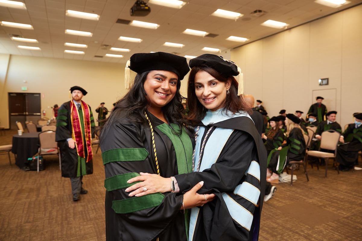 052623_WUHS_0073 Two people smiling at the camera while giving each other a side hug. Both are wearing academic regalia.