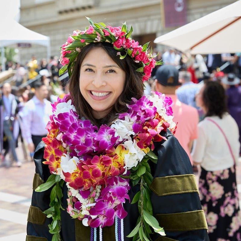 A smiling graduate wearing several colorful orchid leis on her neck and one beautiful pink and green one as a crown.
